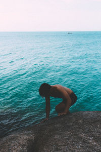 Rear view of shirtless man in sea against sky