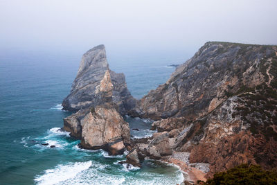 Rock formation on sea shore against sky