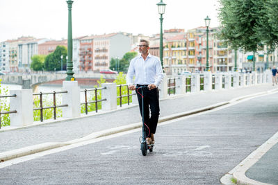 Young businessman in a suit riding an electric scooter while commuting to work in city