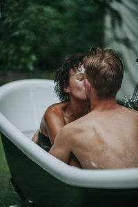 Rear view of shirtless man sitting in bathroom