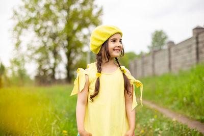 A happy charming little girl in a yellow beret and a yellow dress, stand in nature in the spring