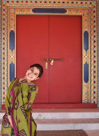 Portrait of smiling young woman standing against door