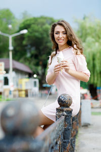Smiling woman with ice cream sitting on railing