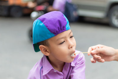 Cropped hand of mother feeding lollipop to son standing on road