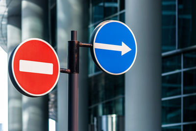 Road signs against modern glass building background, no entry and arrow traffic signs