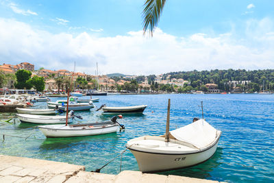 Boats moored on sea by trees and houses against sky