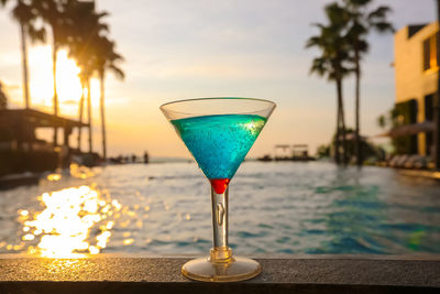 Close-up of drink on table by swimming pool against sky during sunset