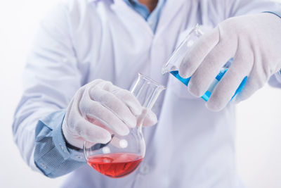 Midsection of scientist pouring chemical in flask against white background