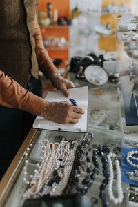 Midsection of male entrepreneur writing in diary while standing at store