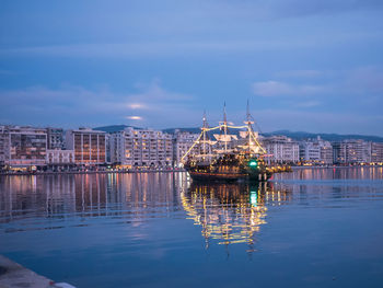 Sailboats in lake by illuminated buildings in city against sky