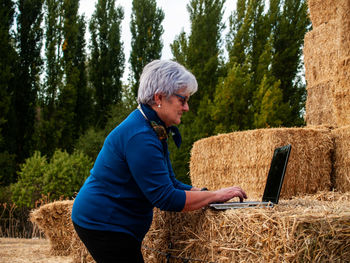 Woman using laptop on hay bales at field