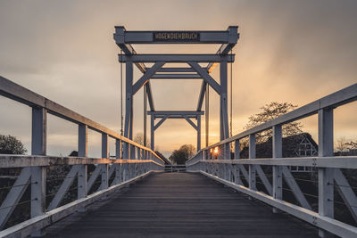 Footbridge against sky at sunset