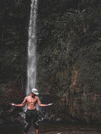 Rear view of shirtless man standing against waterfall