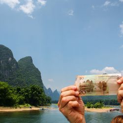 Cropped hands holding paper currency against river and rock formations