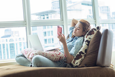 Woman using mobile phone while sitting on window