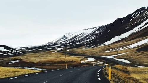 Road amidst snowcapped mountains against clear sky