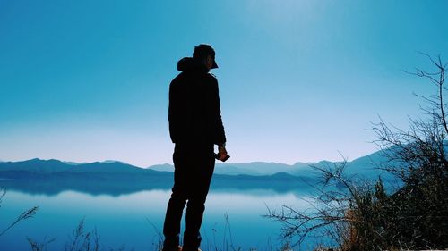 Man standing at lakeshore against sky