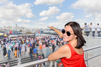 Portrait of woman wearing sunglasses pointing while standing by railing