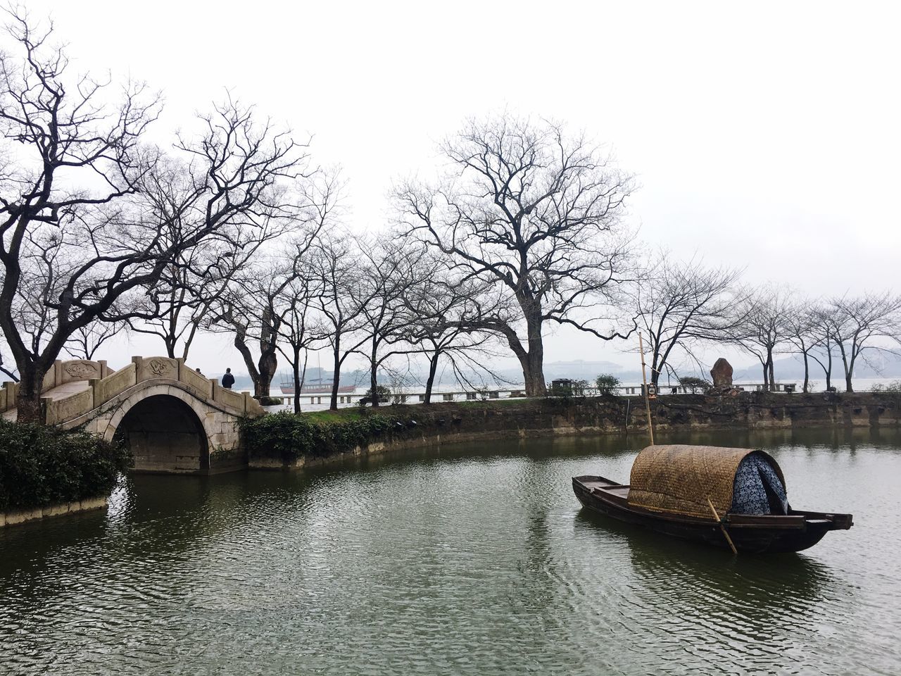 BOAT IN RIVER AGAINST BARE TREES