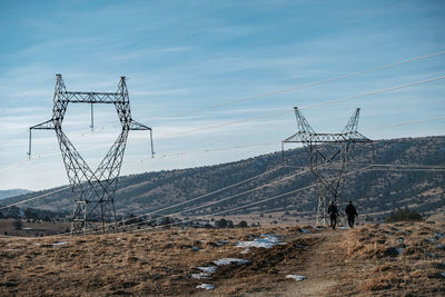 High voltage power lines and road in front against mountains and blue sky