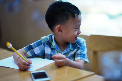 Smiling boy writing in book while sitting at table