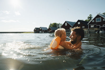 Side view of smiling daughter with father in lake during vacations