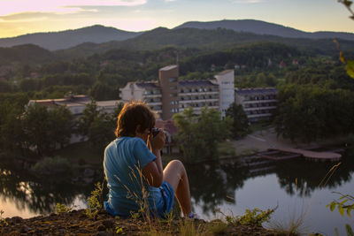 Rear view of boy photographing while sitting on mountain