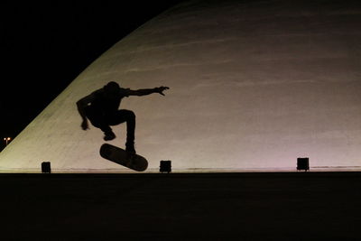 Silhouette man jumping on skateboard at night