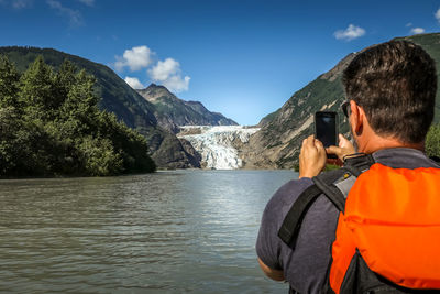 Rear view of man photographing mountains through mobile phone