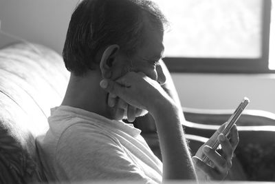 Close-up of mature man using smart phone on sofa at home