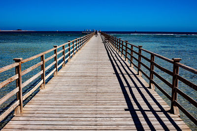 Pier over sea against clear blue sky