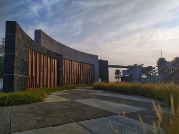 Footpath by building against sky during sunset