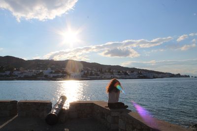 Rear view of woman standing by sea against sky during sunset