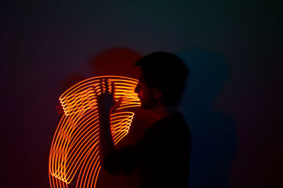Silhouette man standing by illuminated lighting equipment at night