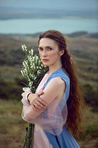 Woman stands on a mountain cliff in a blue long dress in summer