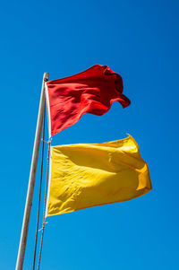 Low angle view of flags waving against blue sky