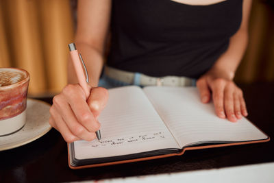 Midsection of woman writing in book at table