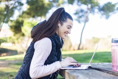 Side view of young woman using laptop while sitting in park