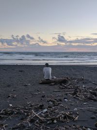 Rear view of man sitting on beach against sky