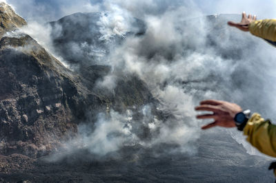 Midsection of person by waterfall against mountain