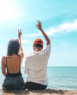 Rear view of people gesturing while sitting at beach against sky