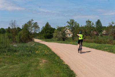 Rear view of man riding bicycle on dirt road