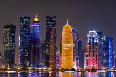 Illuminated buildings of doha city against sky at night