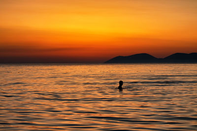 Silhouette man in sea against orange sky