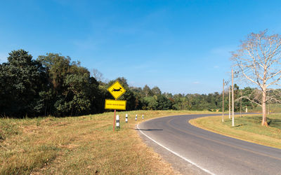 Road sign by trees on field against sky