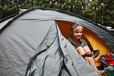 Woman relaxing in tent at camping during vacations. female using smartphone while video call
