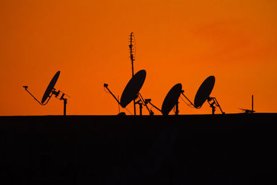 Silhouette of satellite dishes against clear sky during sunset