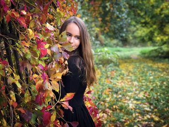Portrait of young woman standing near a wall of colorful red and yellow ivy