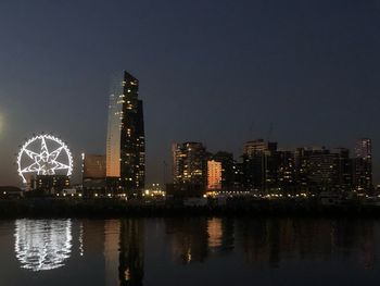 Illuminated buildings by river against sky at night