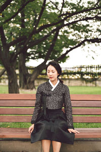 Thoughtful beautiful woman sitting on bench against trees in park